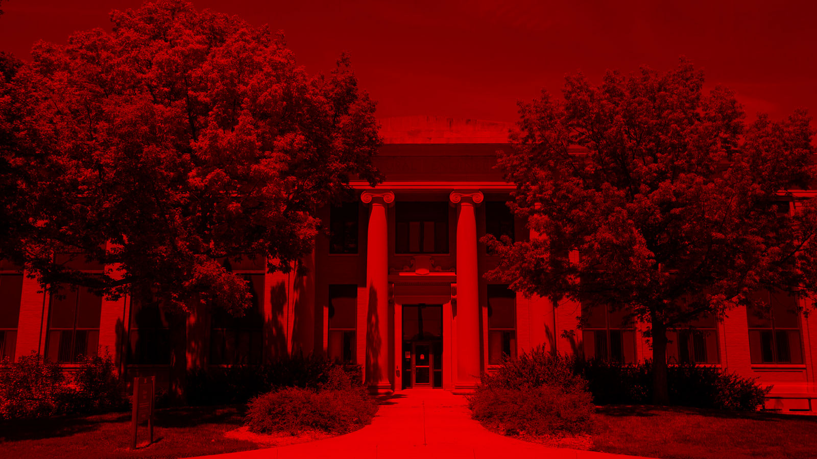 A building entrance with columns, surrounded by trees, tinted entirely in red.