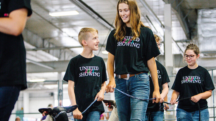 Josh Layman, showman, leads his lamb as a member of the Unified Showing 4-H Club, accompanied by buddy Tatum Terwilliger.