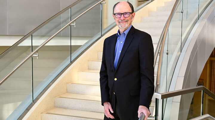 A man stands on a staircase next to a chrome railing and glass encasement.