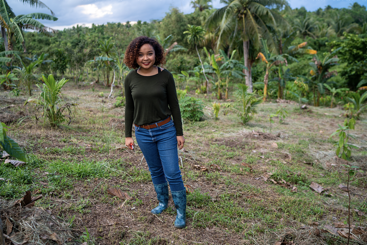 Louise Mabulo stands in front of trees and plants of the agricultural area of the Philippines where she works in sustainable agriculture in cacaor